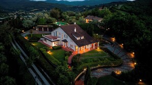 A large, white, two-story house with a red roof, surrounded by well-maintained gardens and a stone pathway. - Villa Ninfeo 10+4, Emma Villas (Arezzo)