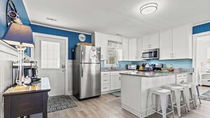 A modern kitchen with white cabinets, a stainless steel refrigerator, a microwave, and a large island with bar stools. - Ce Chell, Spacious 4 BR Channel Home with Beautiful Channel Views and Floating Dock (NORTH MYRTLE BEACH)