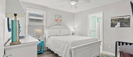 Un dormitorio con cama, escritorio, silla, ventilador de techo y ventana con persianas.
