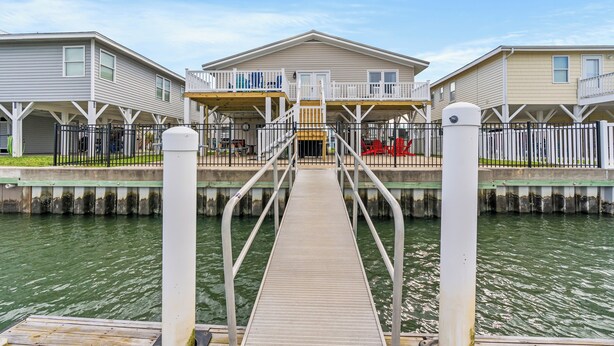 A waterfront property with a dock leading to a house with a balcony and a covered patio. - Ce Chell, Spacious 4 BR Channel Home with Beautiful Channel Views and Floating Dock (NORTH MYRTLE BEACH)