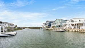 A canal with houses on either side, a boat docked on the left, and a clear sky. - Ce Chell, Spacious 4 BR Channel Home with Beautiful Channel Views and Floating Dock (NORTH MYRTLE BEACH)