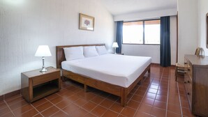 Un dormitorio con una cama de madera, dos mesitas de noche con lámparas, un ventilador de techo, una ventana con cortinas y un aparador.