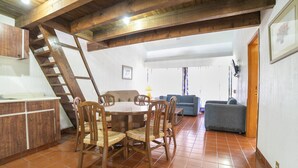 Un comedor con mesa y sillas de madera, una escalera, un sofá y una zona de cocina con armarios.