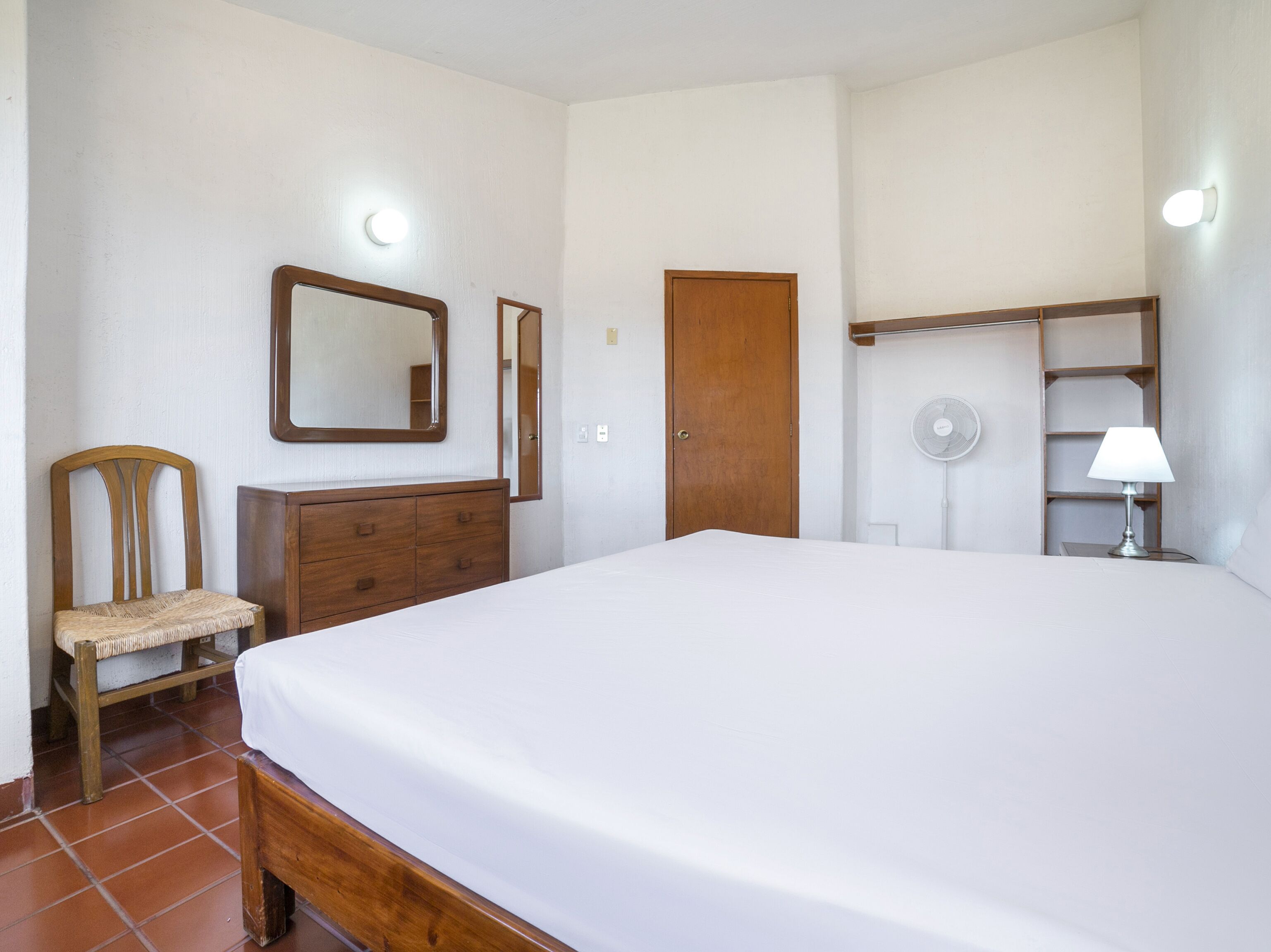 Une chambre à coucher avec un grand lit, une commode en bois, une chaise, une armoire et une table de chevet avec une lampe.