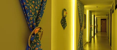 Un pasillo de hotel con cortinas estampadas, un sombrero en la pared y un largo corredor.