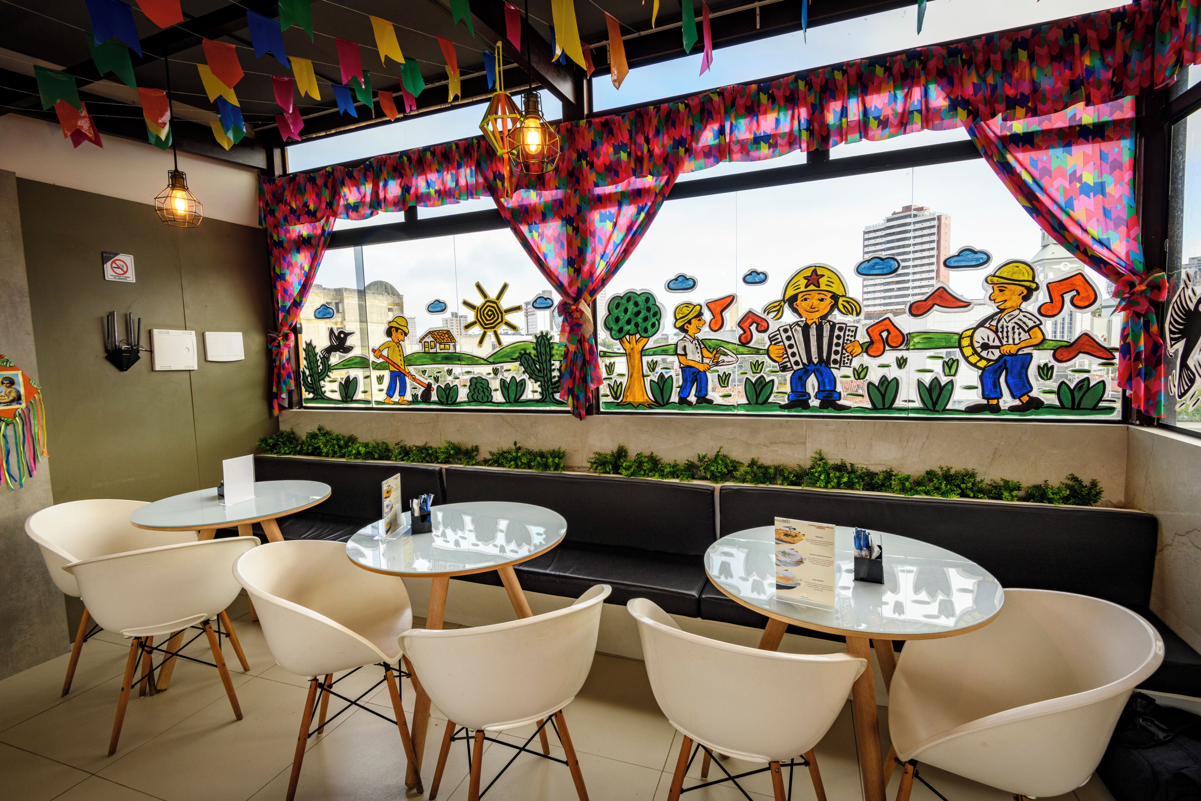 Interior de restaurante com mesas e cadeiras redondas, decorações coloridas e um mural na parede.