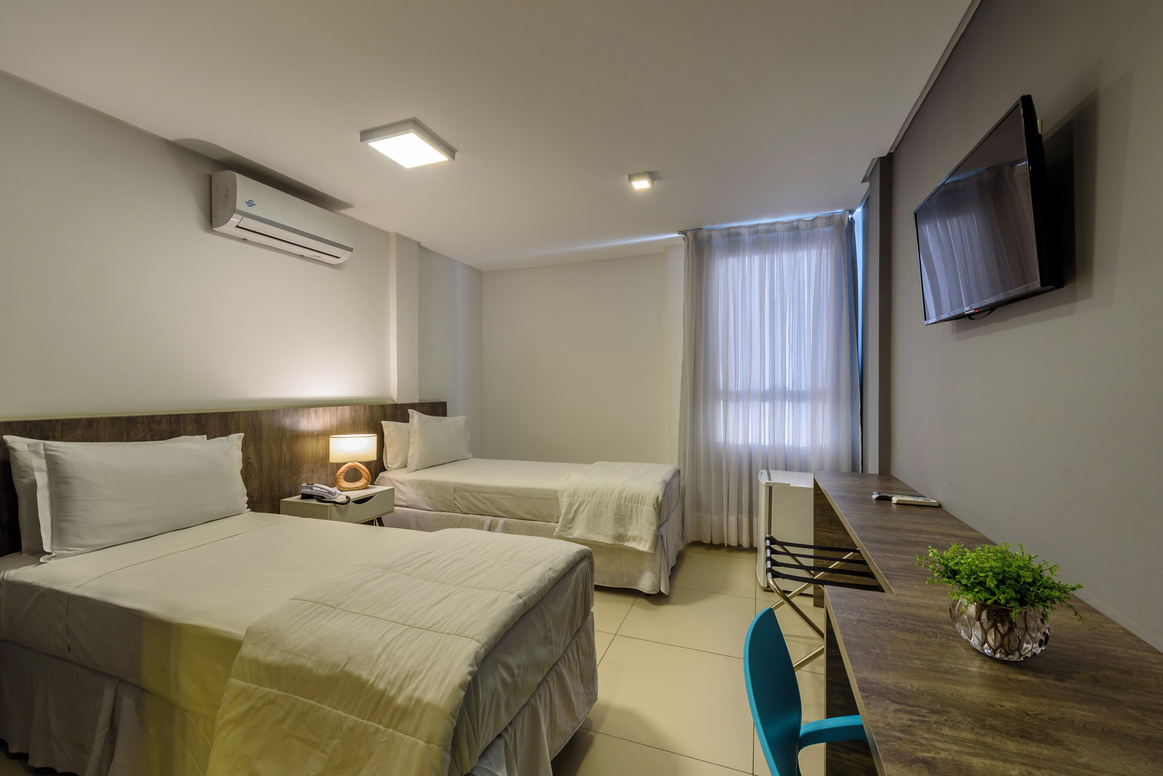 Habitación de hotel con dos camas, un escritorio, una silla, un televisor y un aire acondicionado.