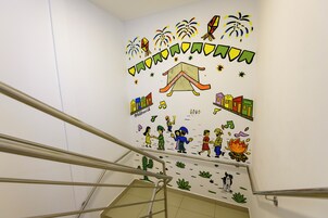 Una escalera con barandillas y una pared con ilustraciones coloridas que incluyen figuras humanas, una casa y notas musicales.