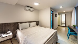 Habitación de hotel con cama, mesita de noche, escritorio, silla y aire acondicionado.