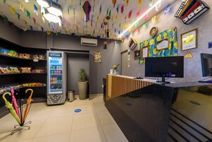 Zona de recepción de hotel con una máquina expendedora, un mostrador de recepción y una pared con certificados.