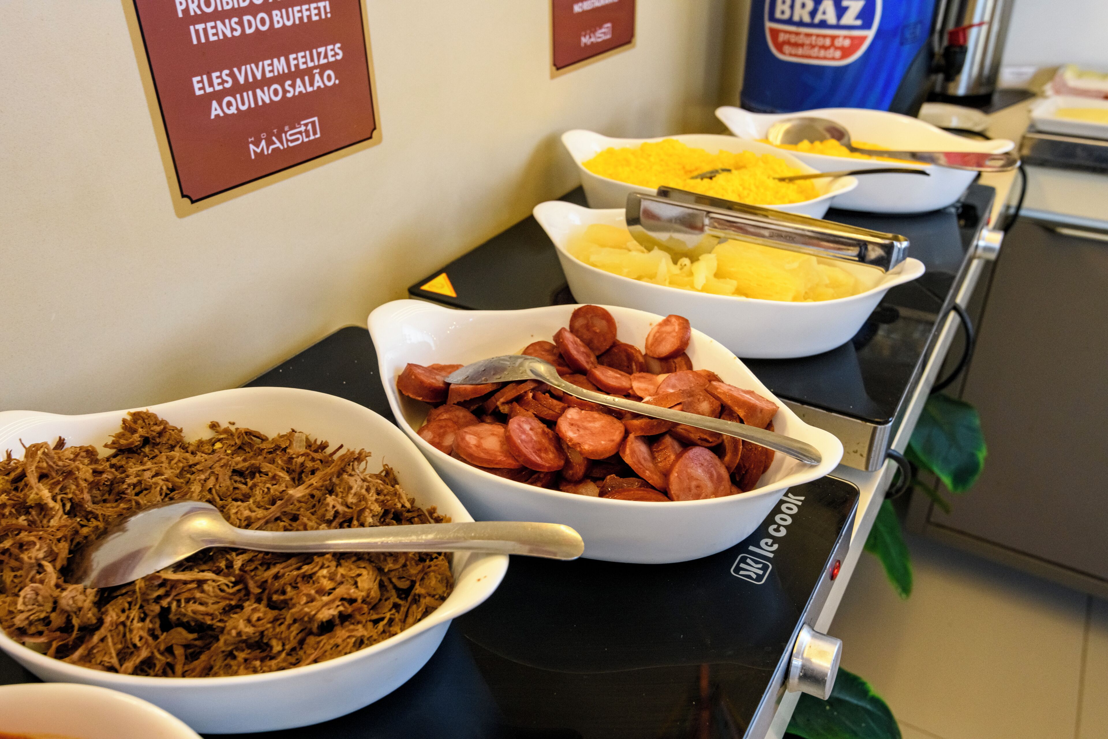 Uma mesa de buffet com diversos pratos, incluindo carne desfiada, salsicha e batatas.