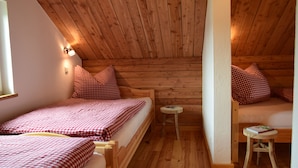 Une pièce chaleureuse avec des murs et un plafond en bois, deux lits avec une literie à carreaux, un petit tabouret et une fenêtre.