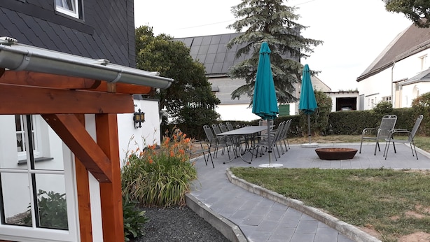 Un espace patio aménagé avec des sièges d’extérieur, un foyer et un jardin agrémenté de plantes et d’un sentier.