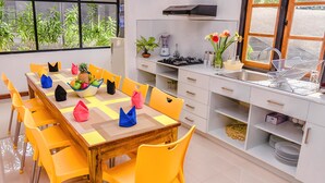 A modern kitchen with a dining area, featuring a wooden table, yellow chairs, a built-in stove, and a window with a view of greenery. - Pinnawala Backpack Residencies (Rambukkana)