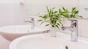 A bathroom with two white sinks, a chrome faucet, and a potted plant. - Pinnawala Backpack Residencies (Rambukkana)