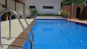 A swimming pool with a metal ladder, surrounded by a tiled patio and a brick wall. - Pinnawala Backpack Residencies (Rambukkana)