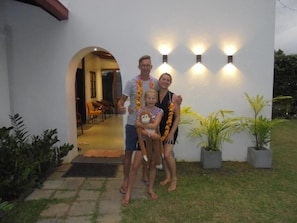 A family standing in front of a building with a paved entrance and potted plants. - Pinnawala Backpack Residencies (Rambukkana)