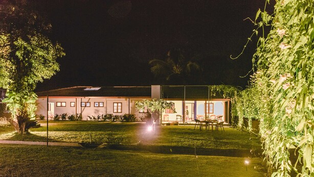 A modern building with a well-maintained lawn, outdoor seating area, and illuminated windows at night. - Pinnawala Backpack Residencies (Rambukkana)