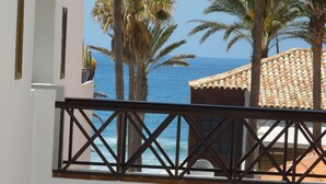 A balcony with a view of the sea, palm trees, and a building with a tiled roof. - Duplex Parque Santiago 2 close to pool, sea + beach, central, Wifi, heated pool (Costa Adeje)