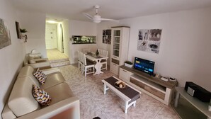 A living room with a sofa, coffee table, TV, and a dining area with chairs and a table. - Duplex Parque Santiago 2 close to pool, sea + beach, central, Wifi, heated pool (Costa Adeje)