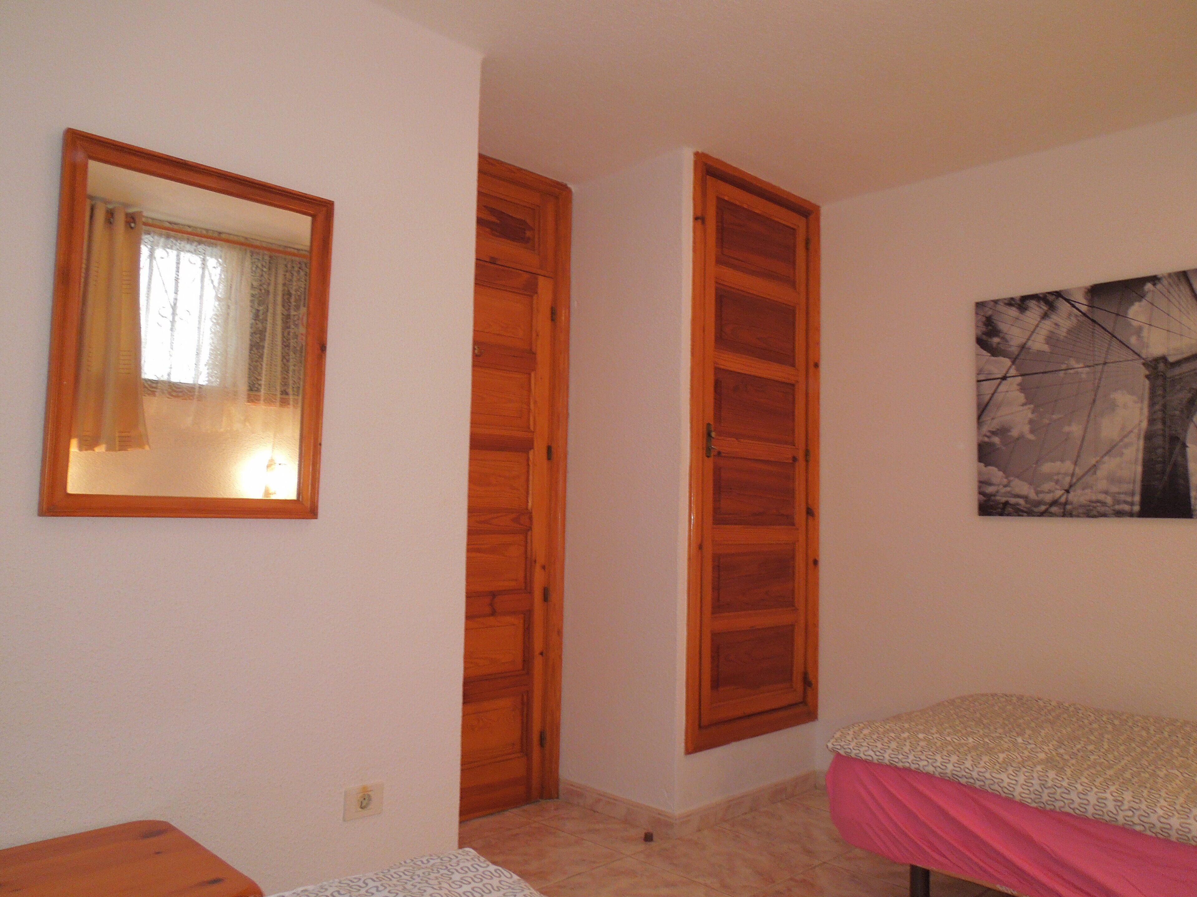 Een slaapkamer met een houten garderobe, een bed met een decoratieve spreideken en een schilderij aan de muur.
