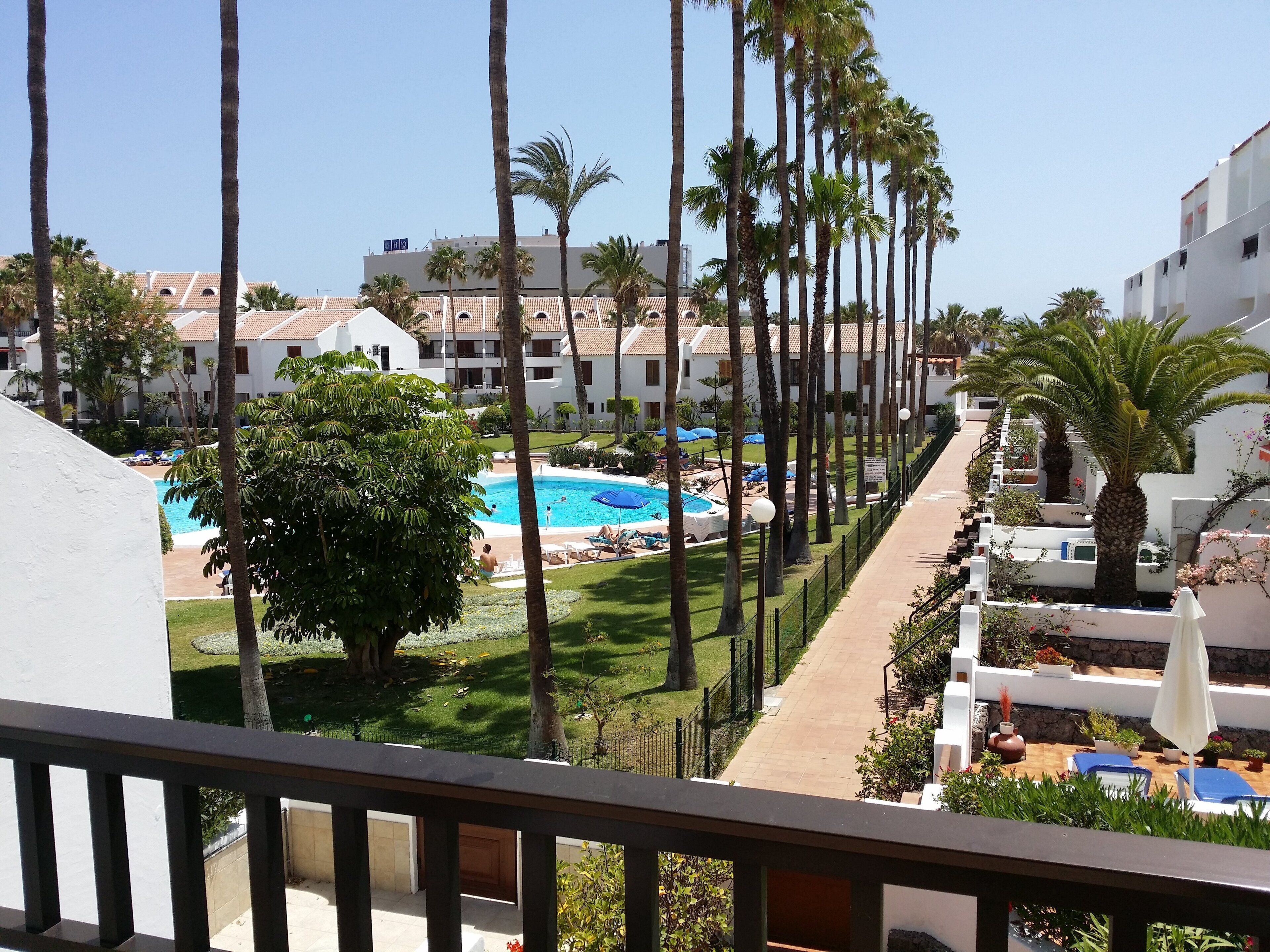 A resort with a swimming pool, palm trees, and a view of the surrounding buildings.