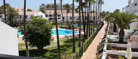 A resort with a swimming pool, palm trees, and a view of the surrounding buildings.