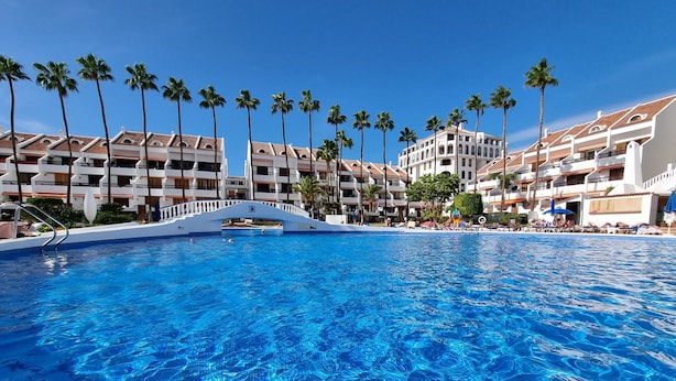 A large swimming pool with clear blue water, surrounded by palm trees and a white bridge. - Duplex Parque Santiago 2 close to pool, sea + beach, central, Wifi, heated pool (Costa Adeje)
