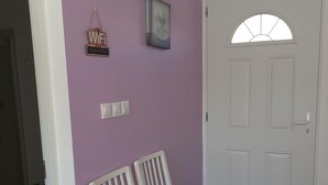 Een hal met een paarse muur, een witte deur en een bankje.