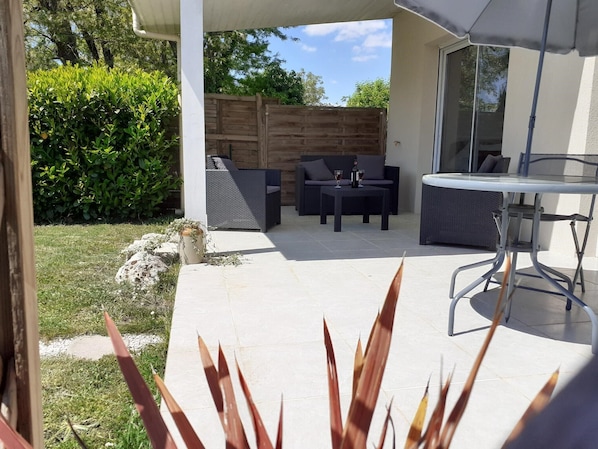 An outdoor patio with a table and chairs, a wooden fence, and a grassy area.