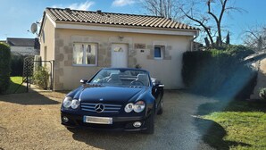 Een blauwe cabrio geparkeerd voor een stenen huis met een pannendak.