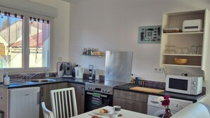 Een compacte keuken met een eethoek, inclusief een koelkast, koffiezetapparaat, magnetron en een kleine eettafel met stoelen.