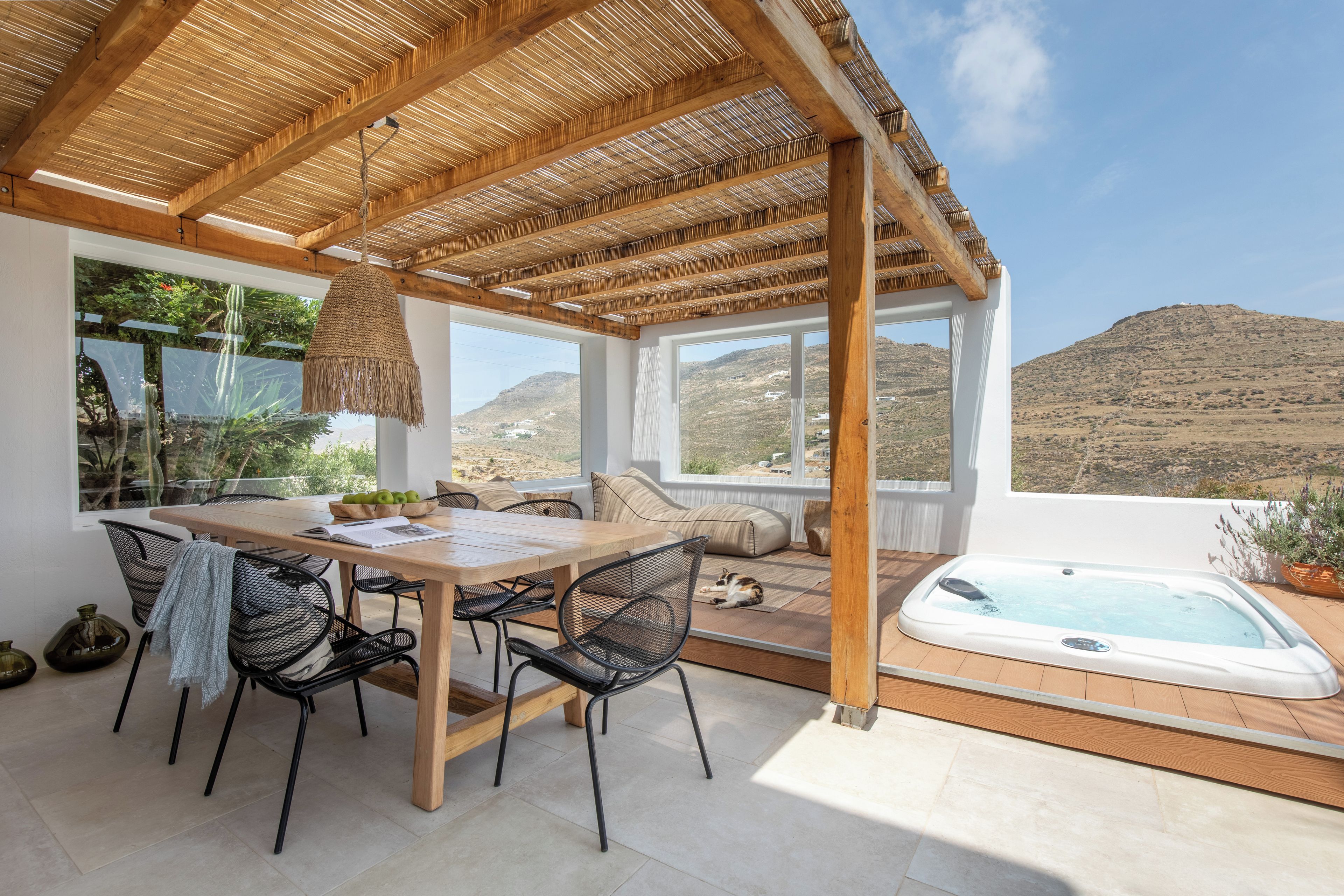 Eine überdachte Terrasse mit Holztisch, Stühlen, einem Whirlpool und Blick auf eine gebirgige Landschaft.