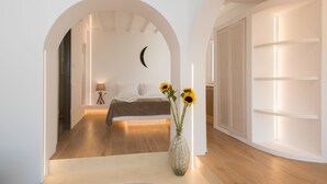 Quarto moderno com piso de madeira, uma cama com manta marrom, mesa de cabeceira com luminária e um vaso com girassóis.