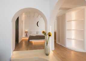 Un dormitorio moderno con suelo de madera, cama con manta marrón, mesita de noche con lámpara y un florero con girasoles.