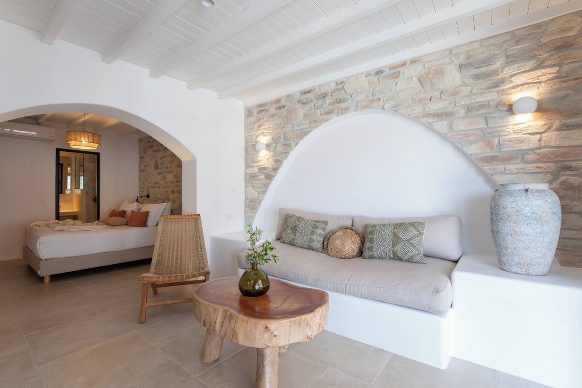 Un intérieur moderne avec un mur en pierre, un canapé, une table en bois ornée d’un vase et un lit avec des coussins.