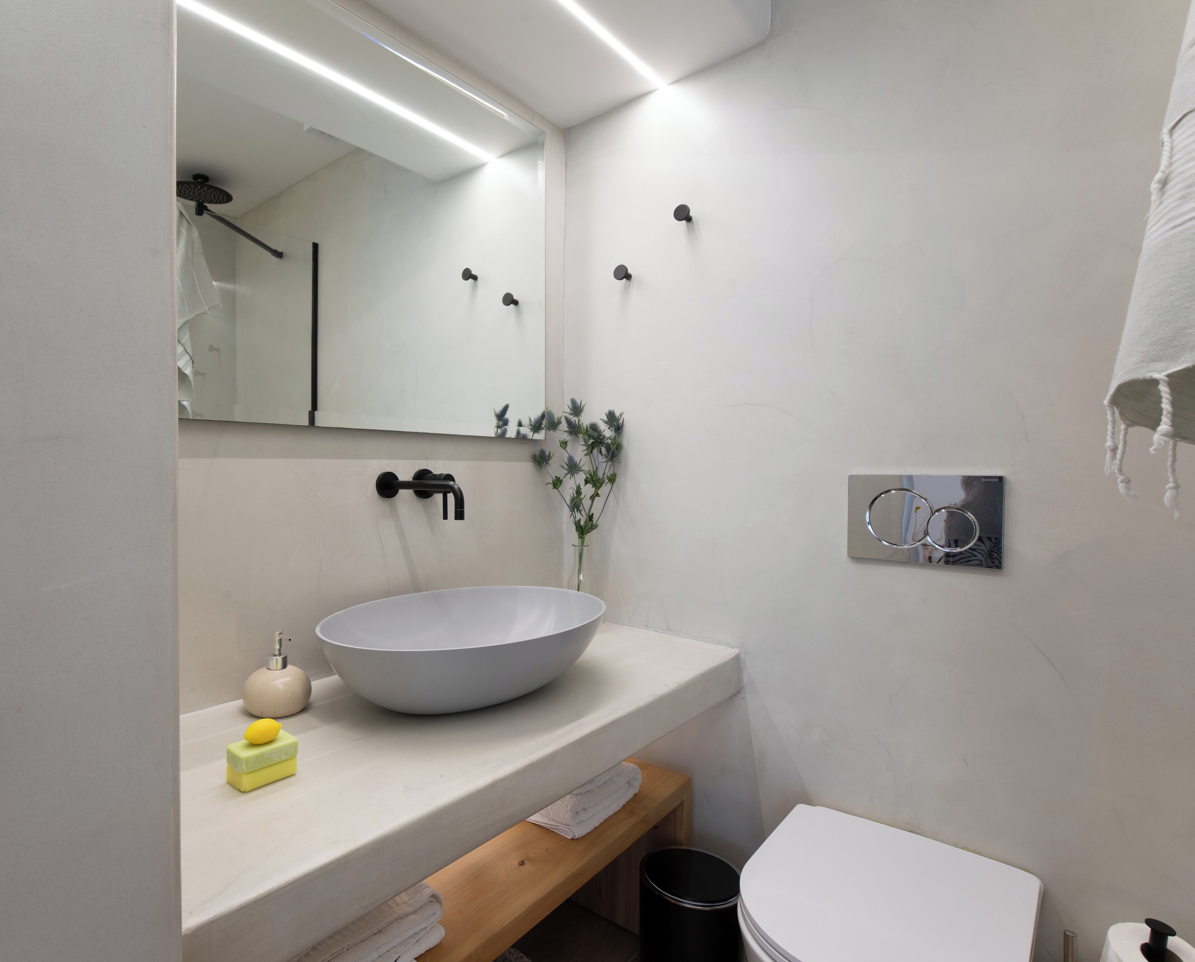 Et moderne badeværelse med en stor, hvid vask, et spejl, et toilet og en lille træbænk.