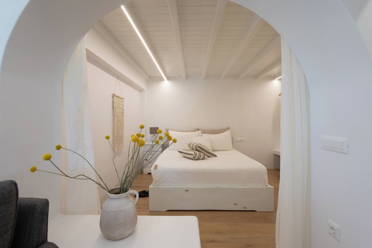 Une chambre à coucher au style minimaliste, avec un lit, un vase contenant des fleurs jaunes et un mur blanc.