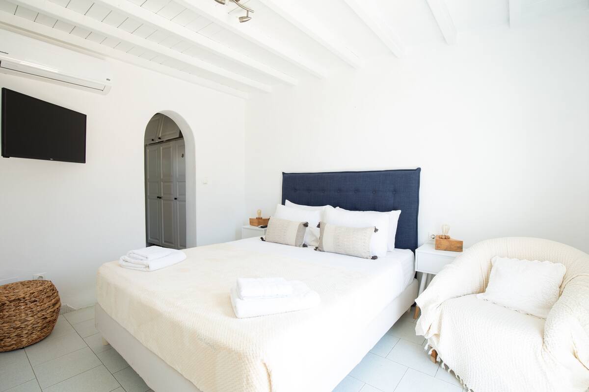 Une chambre moderne avec un grand lit, un téléviseur fixé au mur et un coin salon confortable.