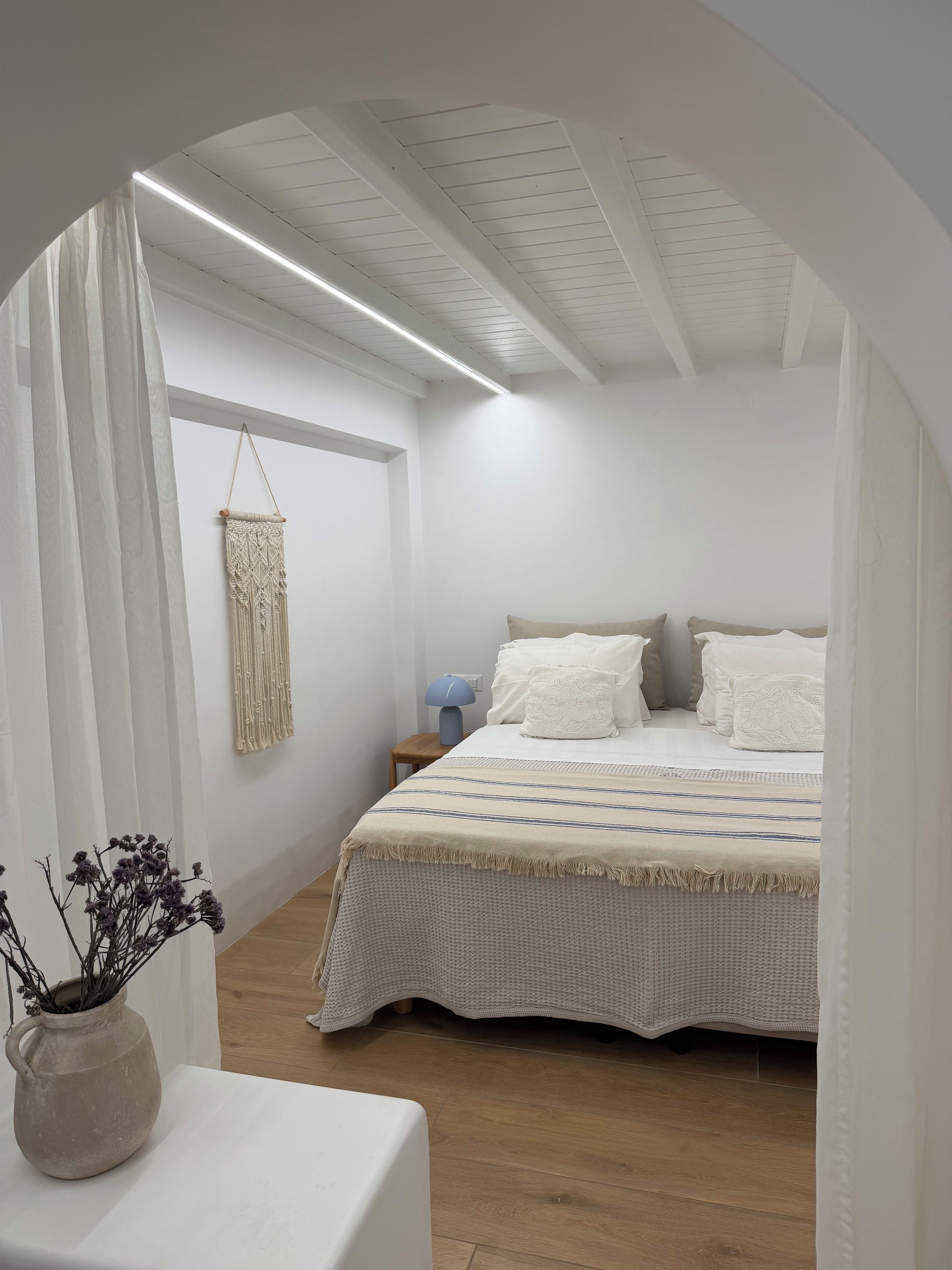 A bedroom with a bed, bedside table, and a macrame wall hanging.
