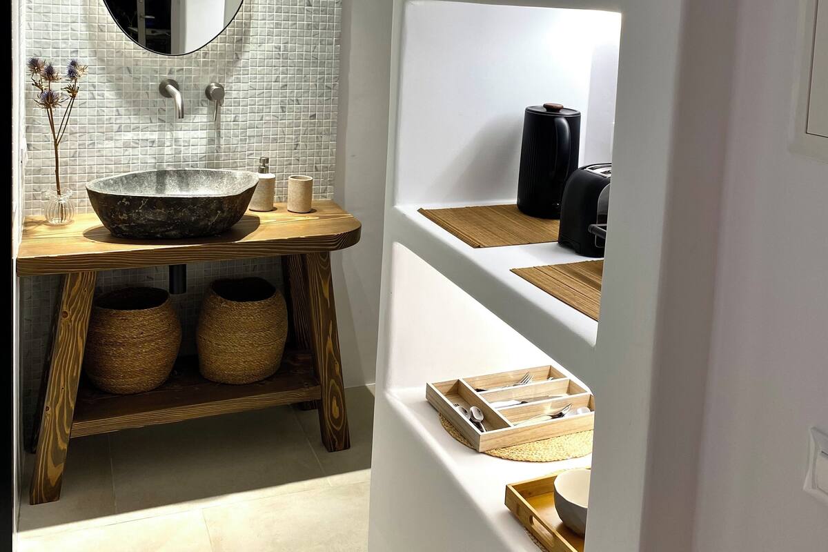 Une salle de bain moderne avec un grand miroir ovale, un meuble-lavabo en bois et des étagères intégrées où sont rangés les produits de toilette.