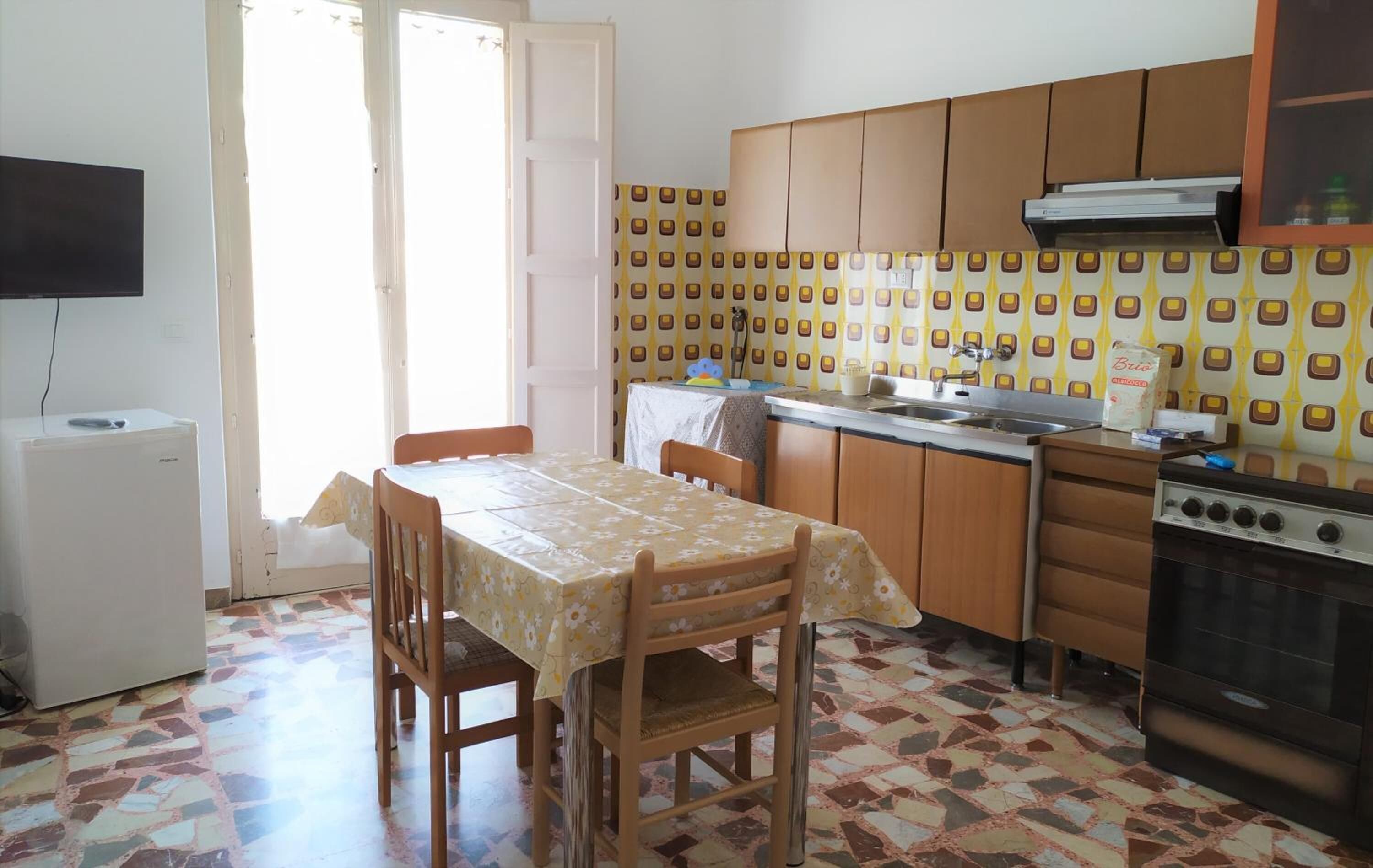 A compact kitchen with a dining table, chairs, a refrigerator, a stove, and patterned tiles.