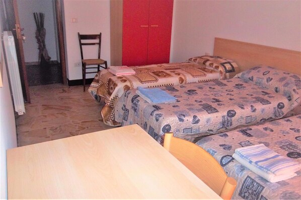 A small room with two beds, a wooden table, and a red wardrobe.