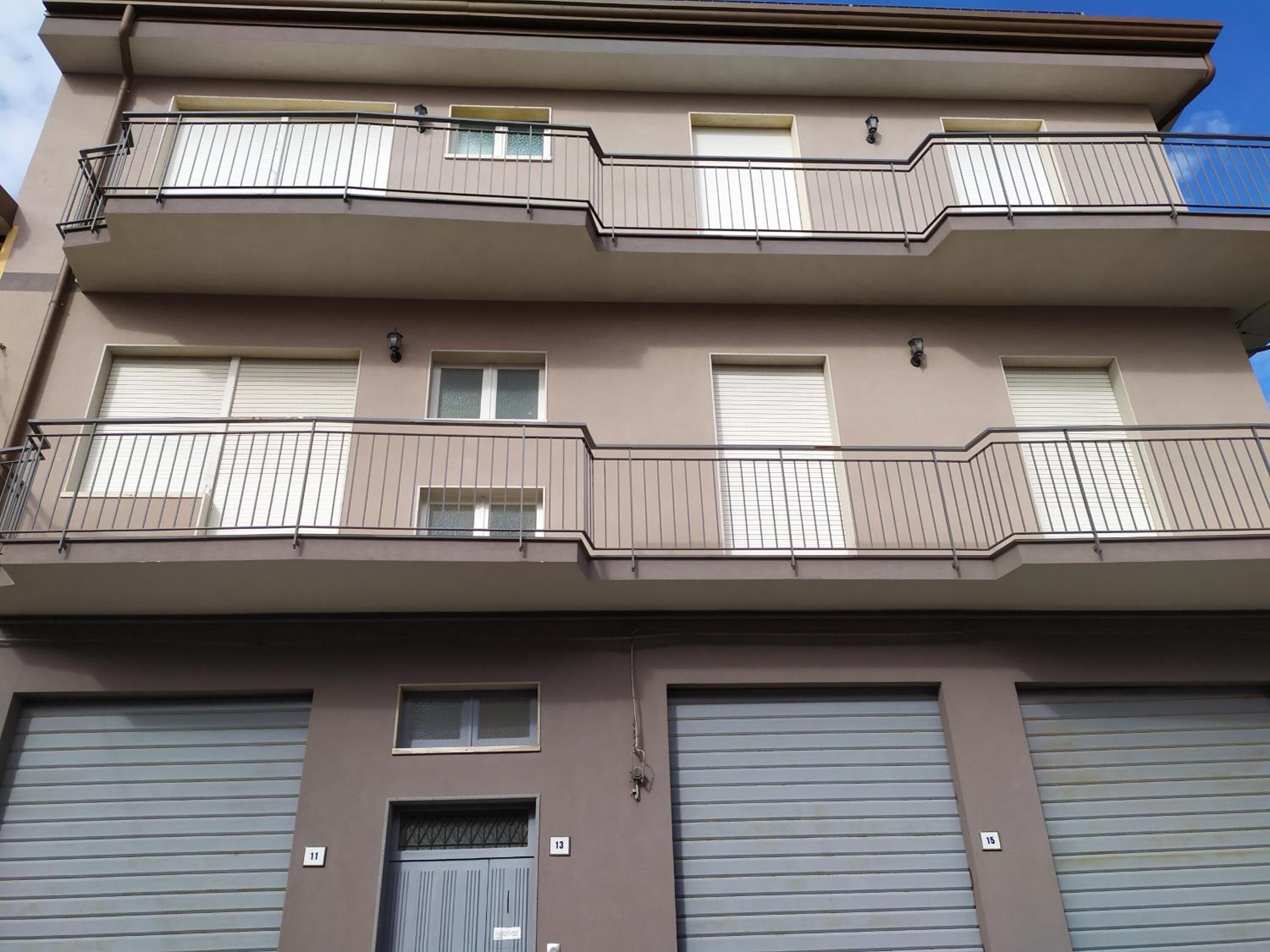 A multi-story residential building with balconies, large garage doors, and a clear sky.