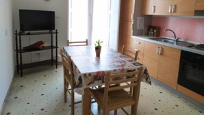 A compact kitchen with wooden cabinets, a dining table with chairs, a television on a stand, and a window with curtains. - Casa Valentina (Linguaglossa)