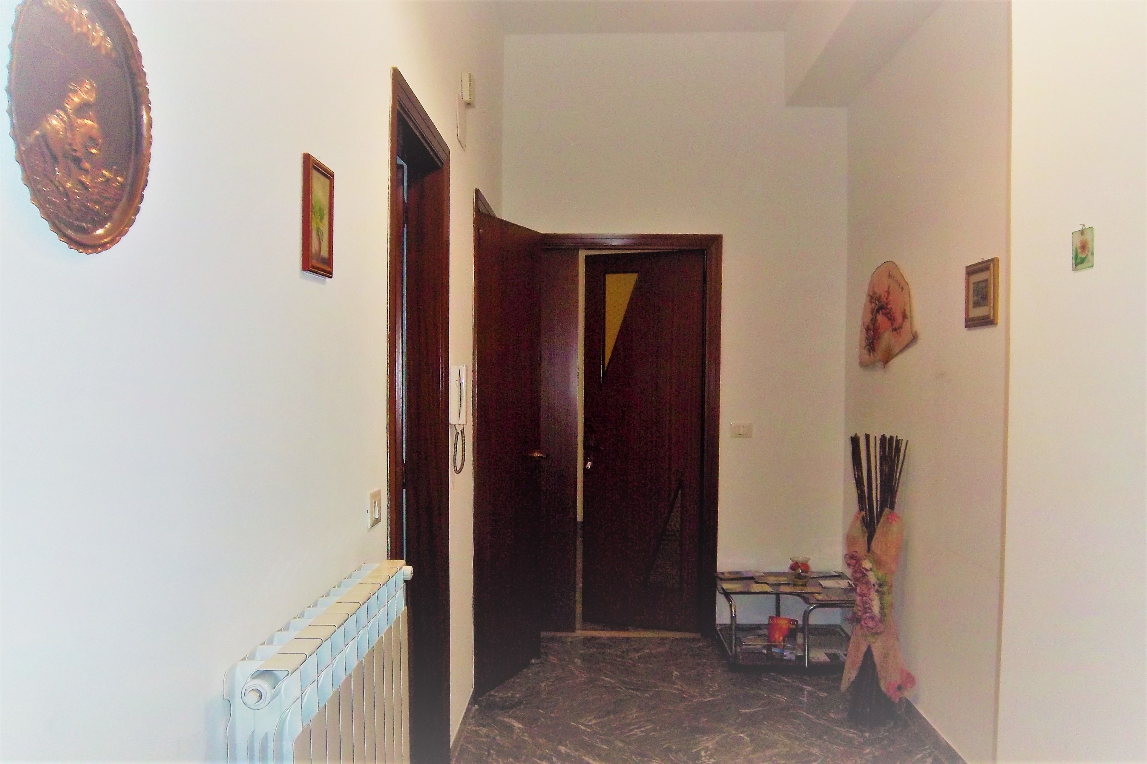 A hallway with a radiator, a wooden door, and a small table with a vase.