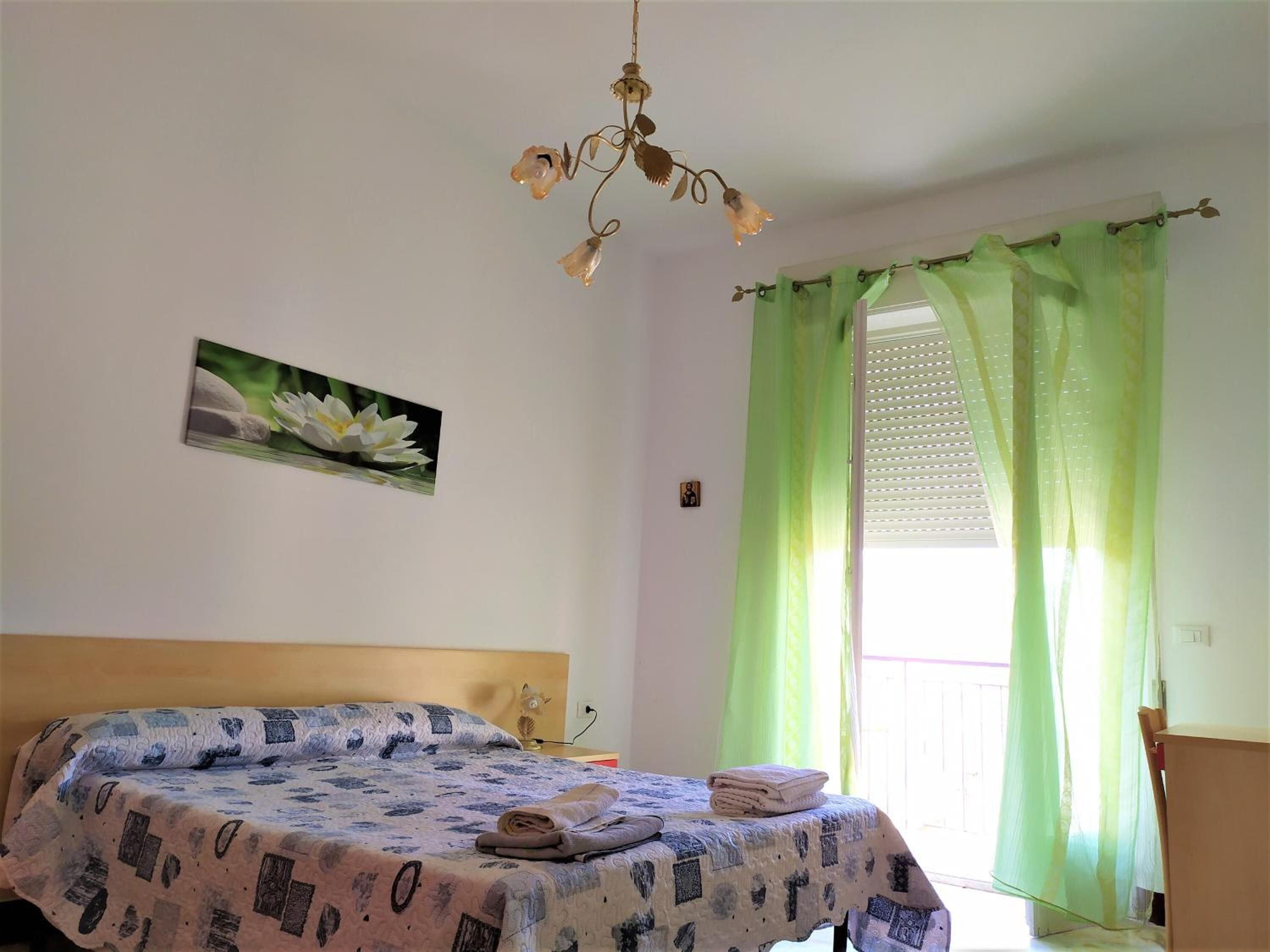 A bedroom with a bed, a painting of a lotus flower, a chandelier, and green curtains.
