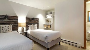 Ein Schlafzimmer mit zwei Betten, einem hölzernen Kopfteil, einem Nachttisch mit Lampe und einem eingebauten Kleiderschrank mit Regalen.