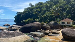 Escena costera con grandes rocas, agua cristalina y una casa con techo de tejas.