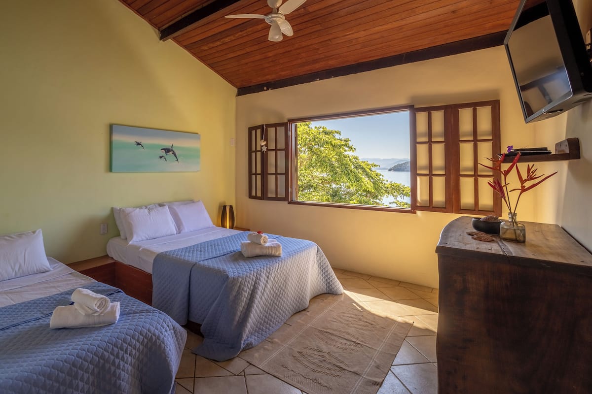 Une chambre avec deux lits, un plafond en bois, une télévision et une fenêtre donnant sur un paysage verdoyant.